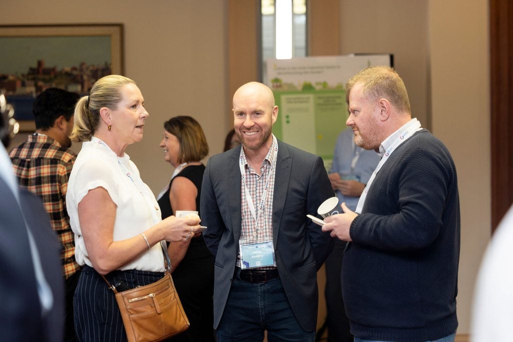 Group of three conference attendees networking and talking informally during a refreshment break.