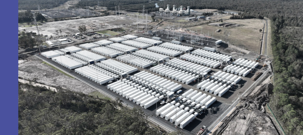 Hundreds of white, rectangular battery container units are tightly packed in rows within a fenced enclosure.