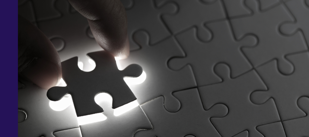 A hand holding the final piece of a puzzle, ready to be placed into a glowing gap in a nearly completed white jigsaw puzzle.