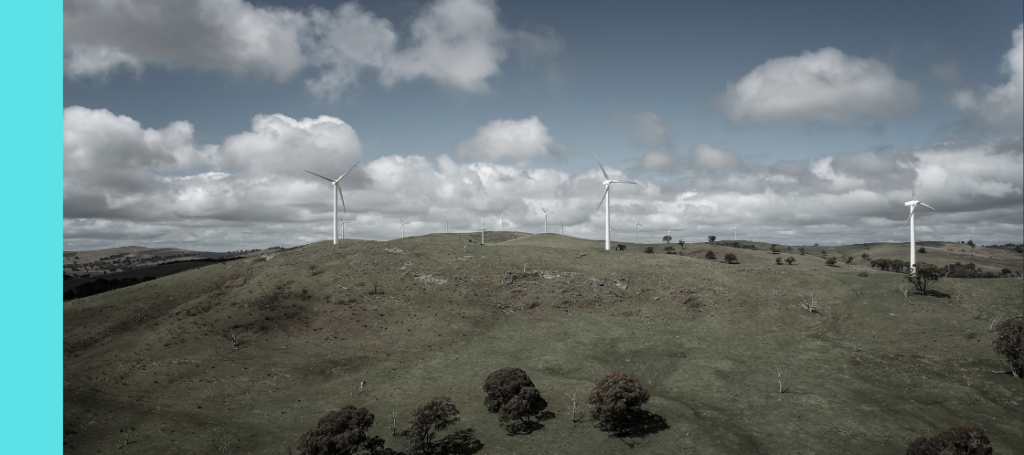 A wind farm located on rolling, grassy hills under a dramatic sky filled with large white clouds.